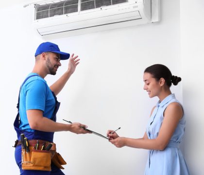 Professional technician speaking with woman about air conditioner indoors